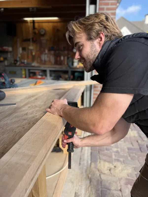 Rick werkt nauwkeurig aan de rand van een houten plank.