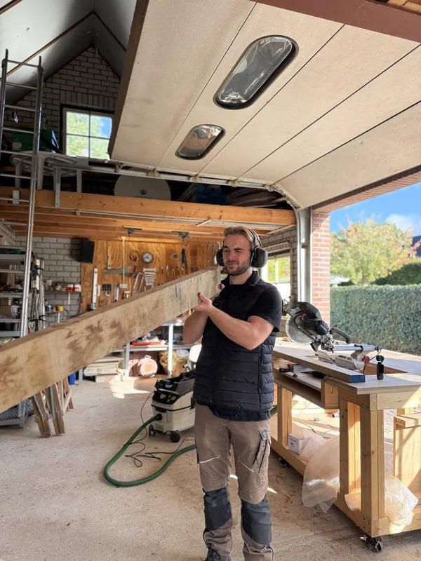 Rick draagt een houten plank in zijn werkplaats.