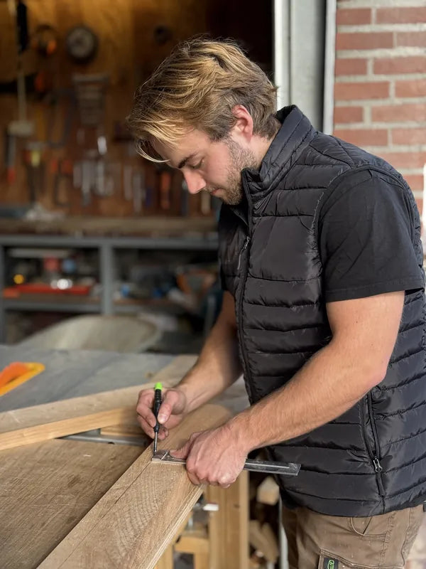 Rick tekent met een winkelhaak een houten plank af.